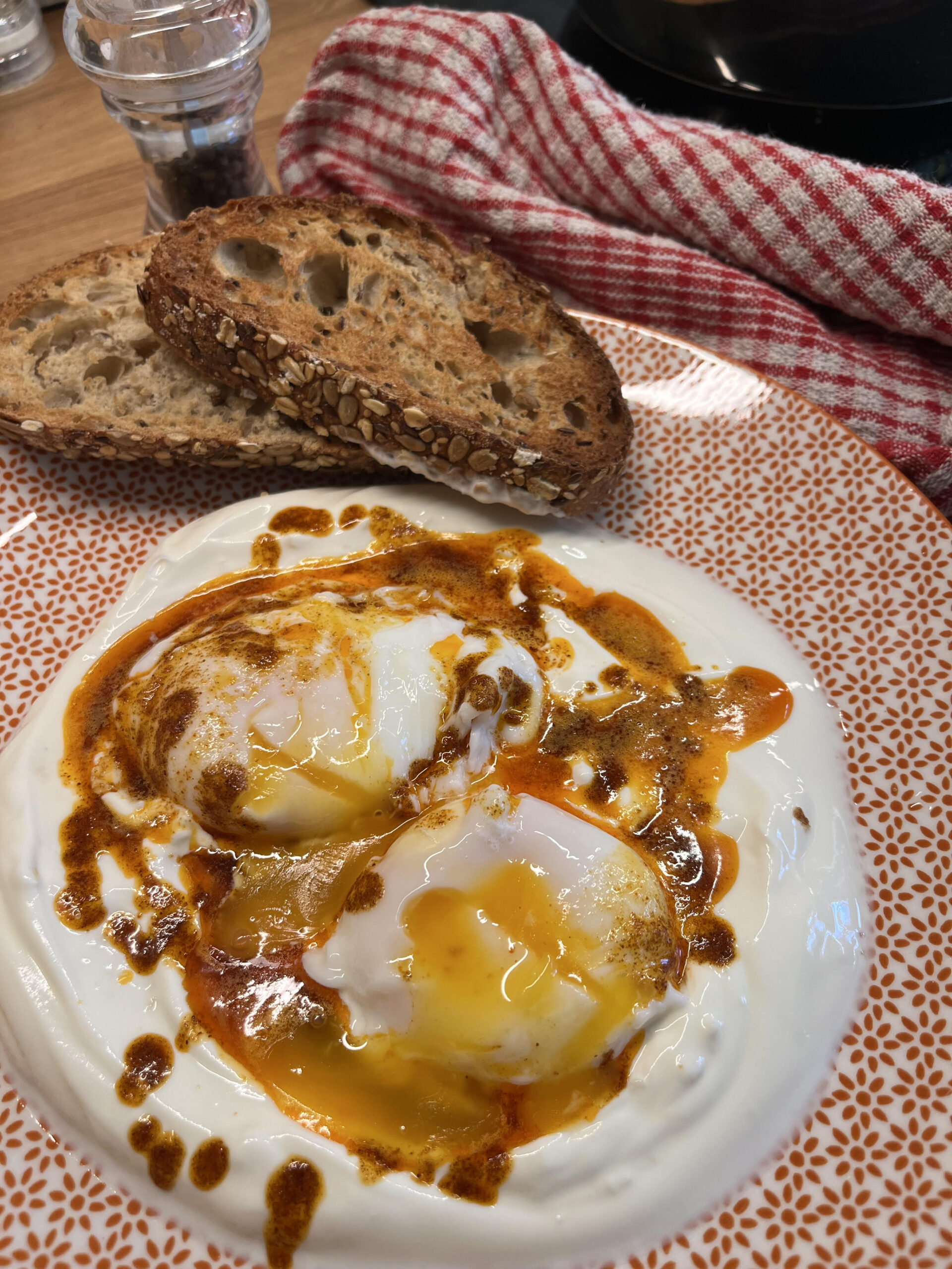 Image of turkish eggs and toast on an orange patterned plate next to a kitchen towel